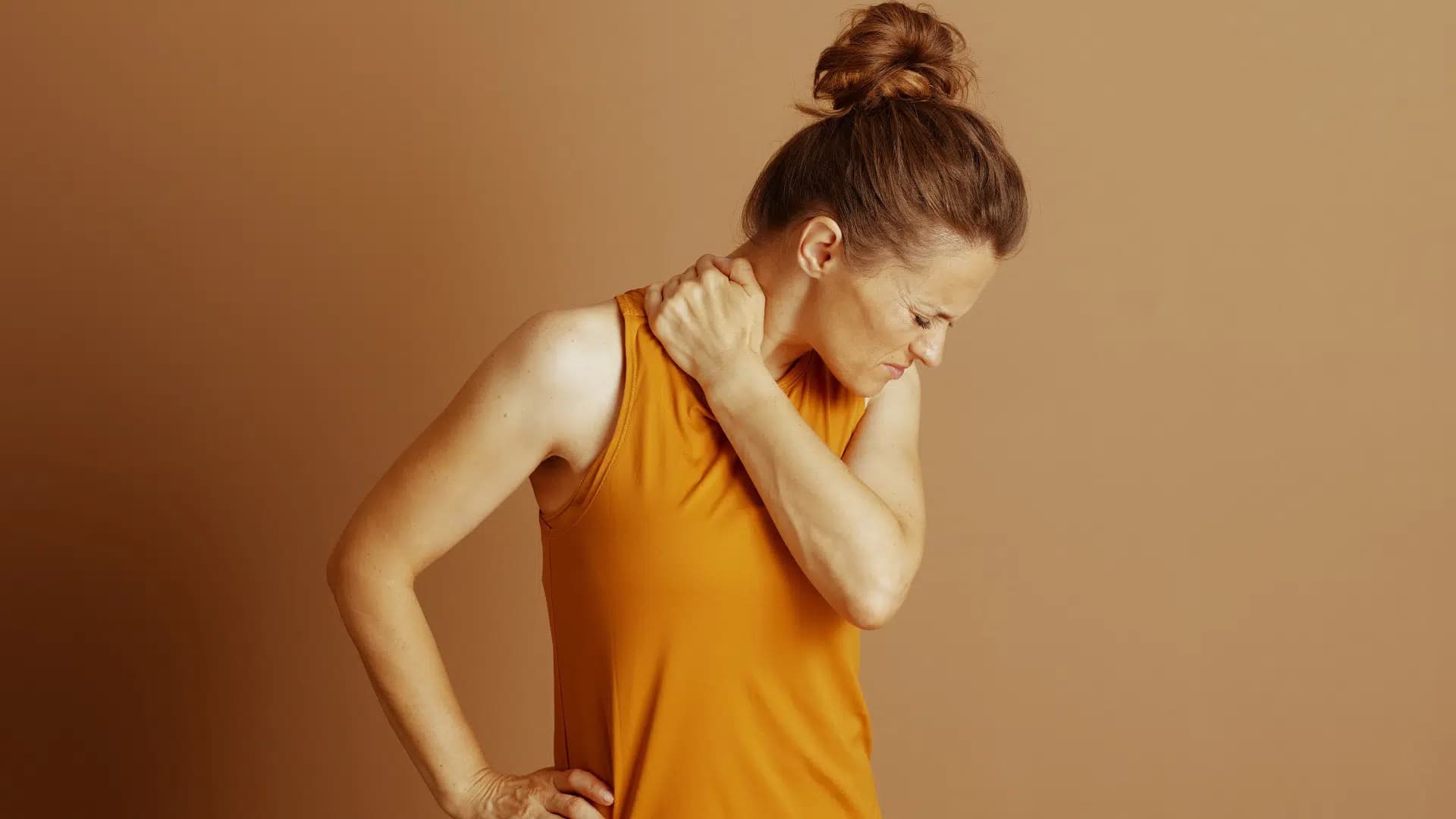 Woman in an orange top looking down and holding the side of her neck