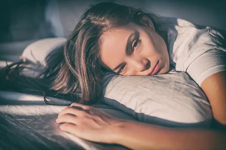 Tired woman lying on her side with her head on a pillow, looking sadly at the camera