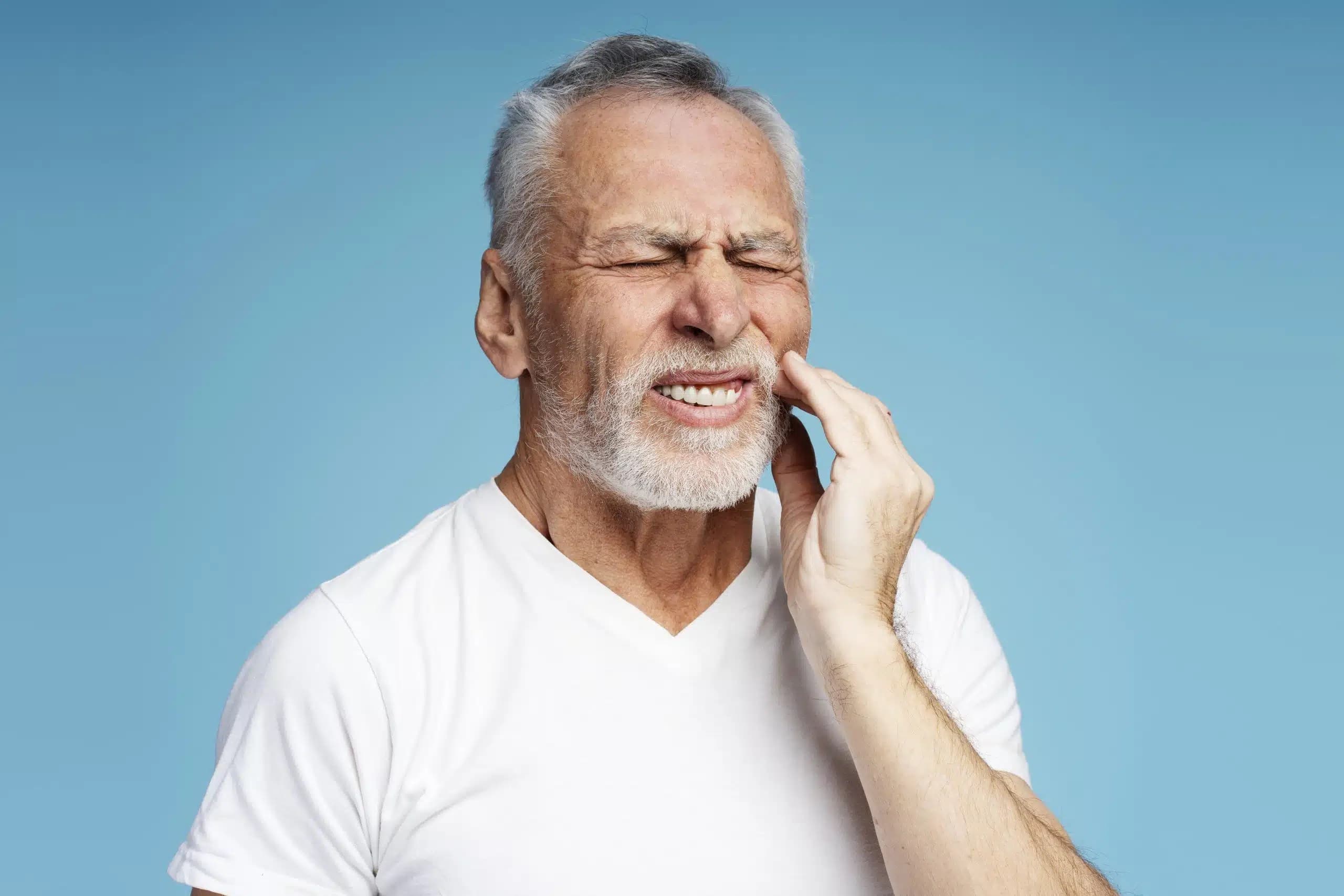 Older man with a gray beard wincing and touching his jaw