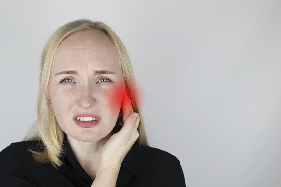 Woman holding her jaw, with the facial pain highlighted in red