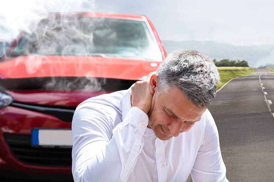 Man holding his neck in front of a damaged car after a collision