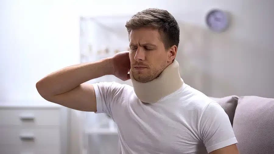 Man in a foam neck brace wincing and holding the back of his neck