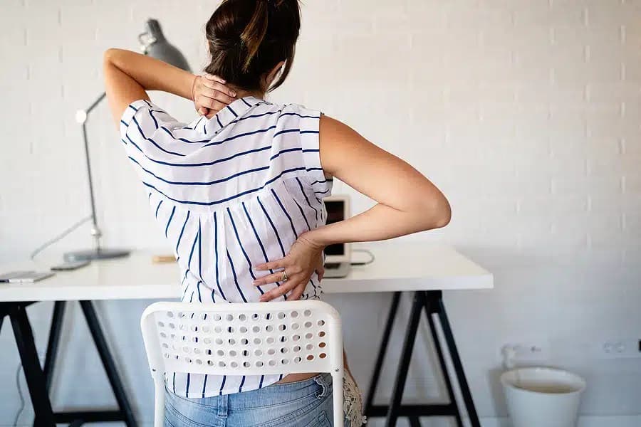 Woman at a desk holding the back of her neck and her lower back