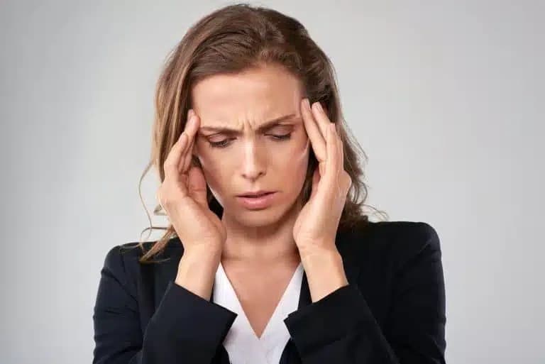 Woman in a dark blazer frowning with her fingertips pressed to her temples