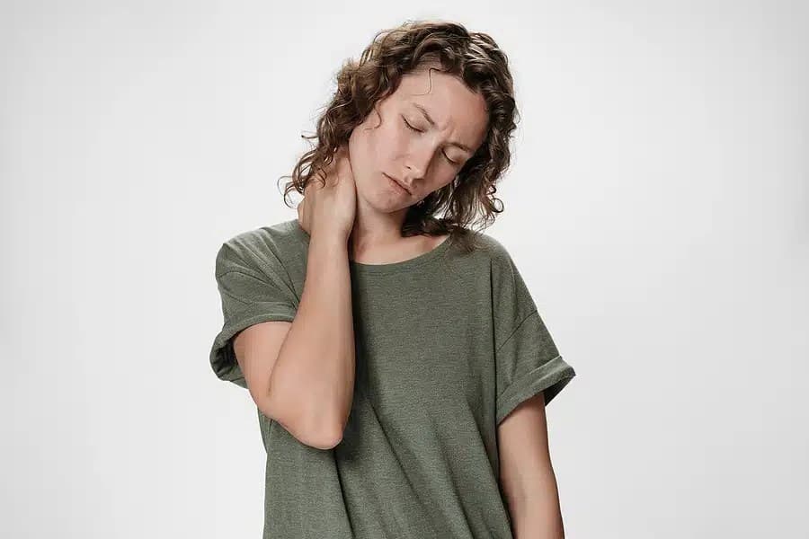 Woman with curly hair, eyes closed, holding the back of her neck