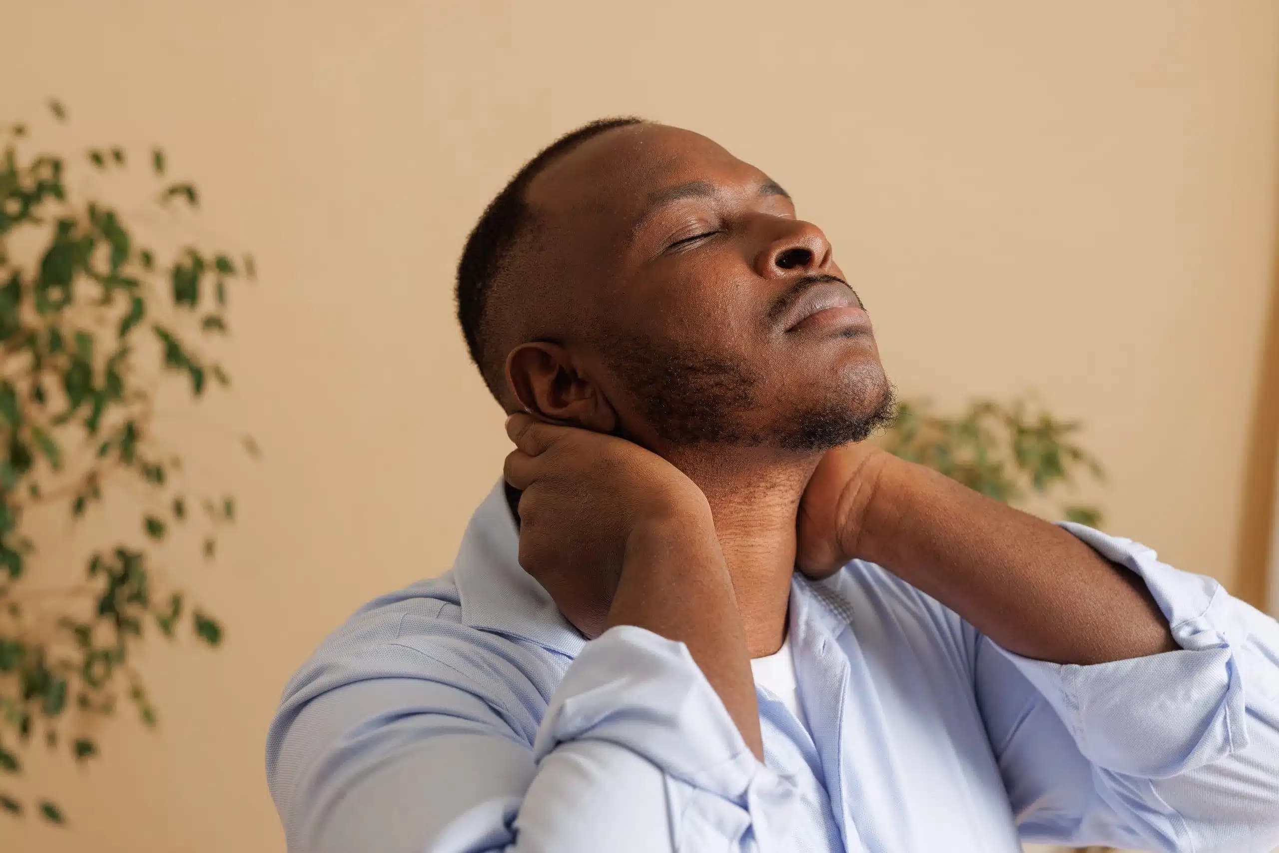 Man with his eyes closed and head tilted back, holding the back of his neck