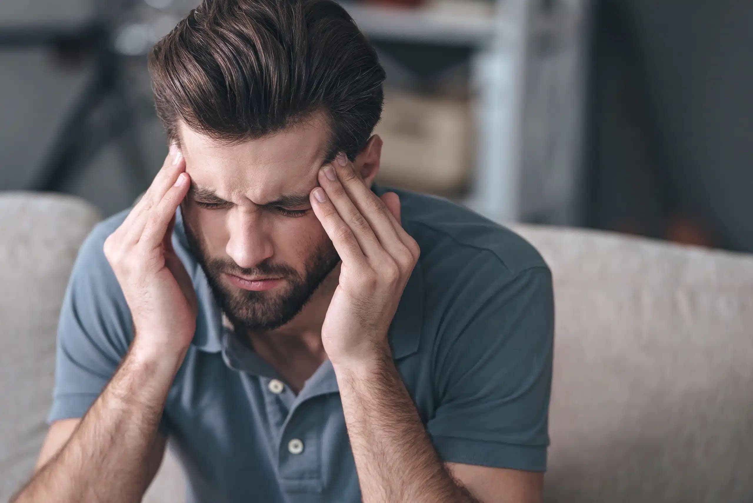 Bearded man on a sofa pressing his temples with a strained expression