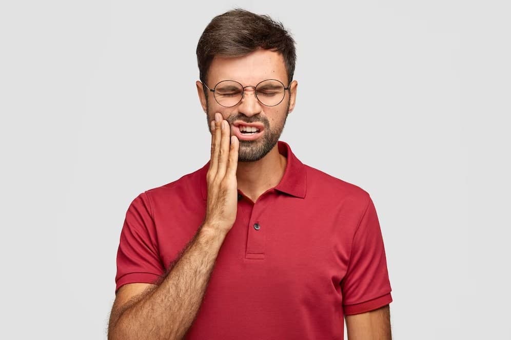 Man with glasses and a red shirt wincing with his hand against his jaw