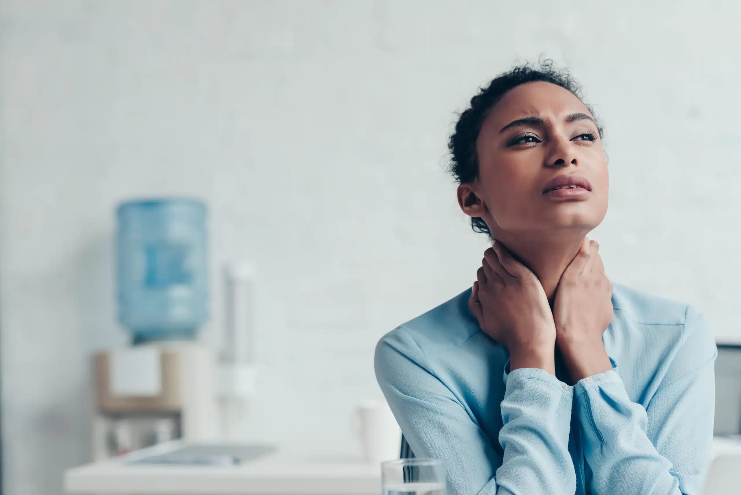 Woman at an office desk with her hands on her neck and a pained expression