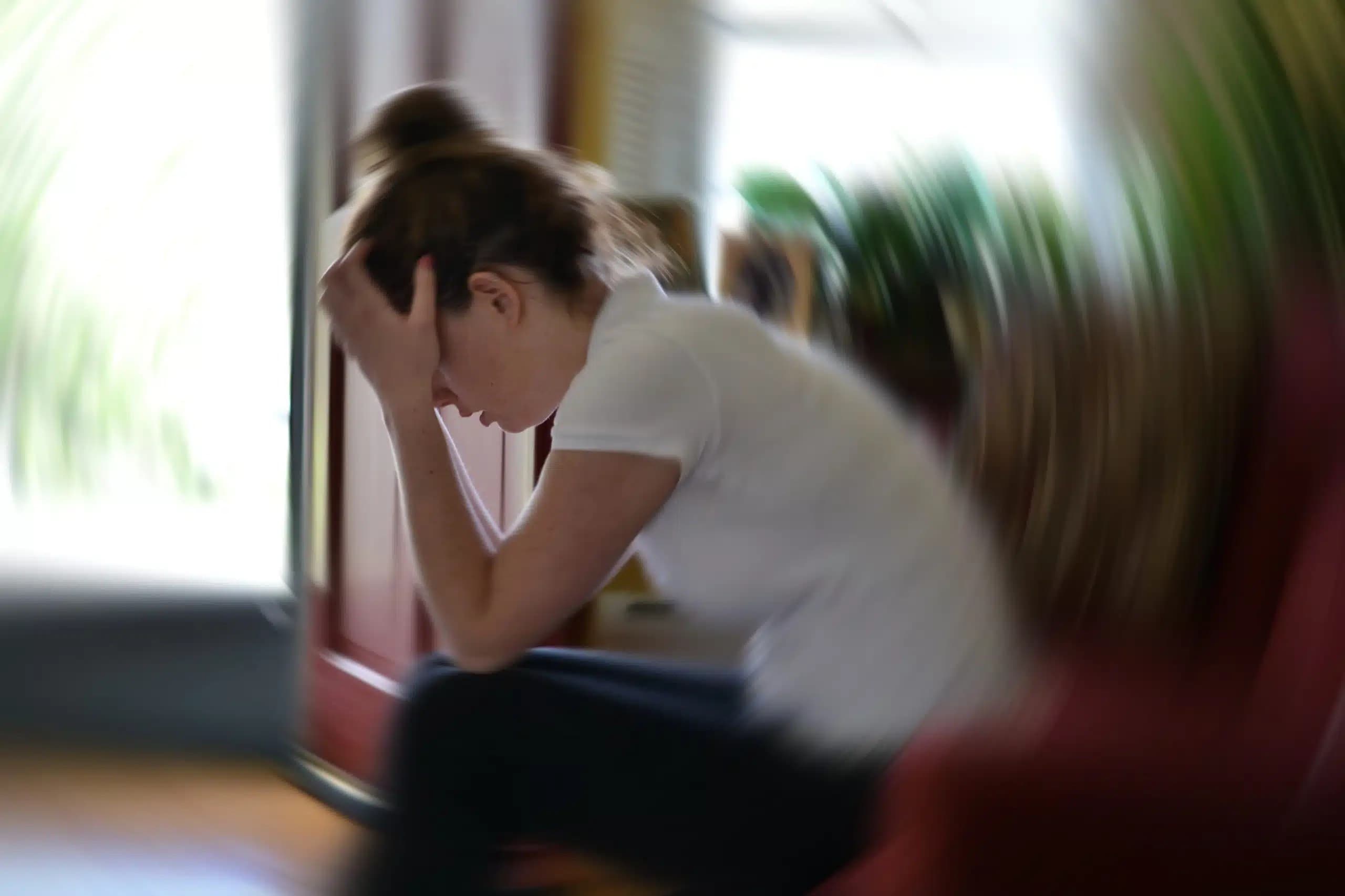 Woman with her head in her hands, with the room blurred in a spinning effect