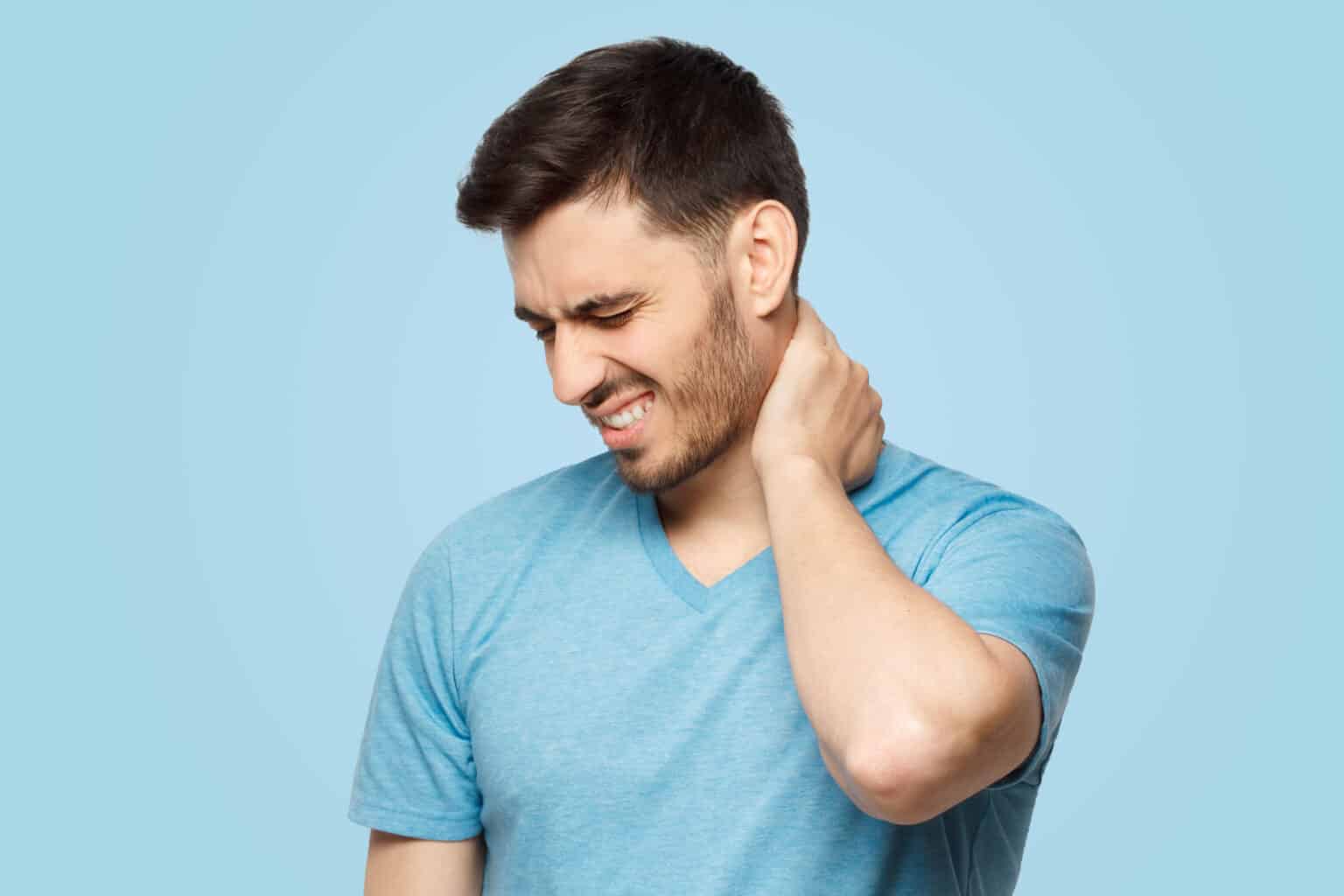 Man in a blue t-shirt grimacing and holding the back of his neck